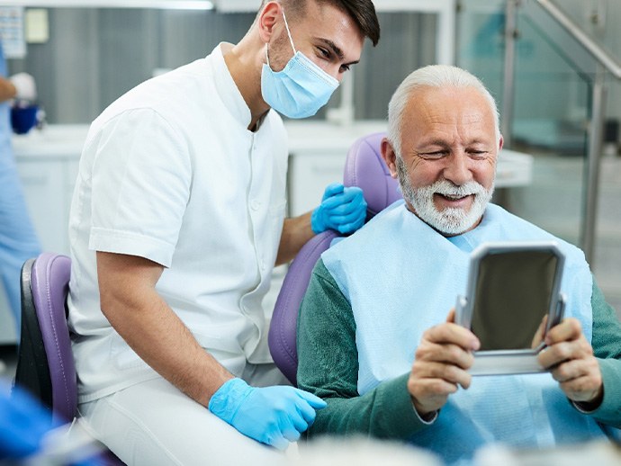 Older man looking at new smile while learning about dental implant post-op instructions in Bethlehem