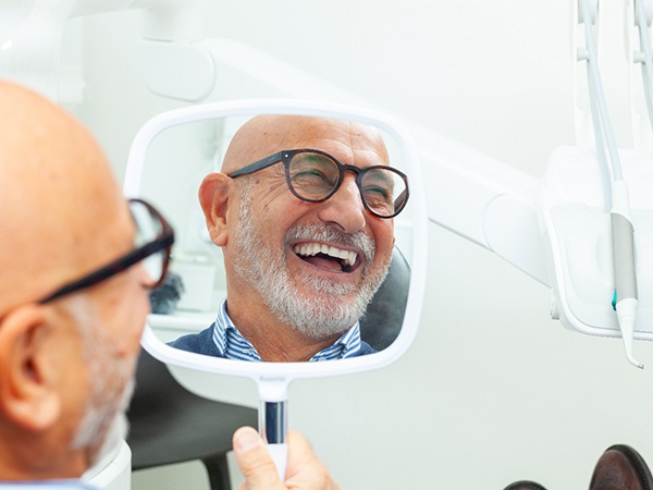 An older man admiring his smile with a hand mirror