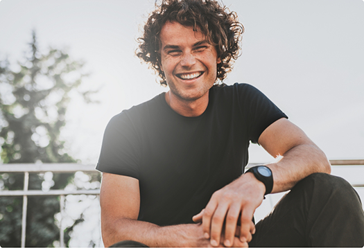 Young man with curly brown hair grinning in the sun