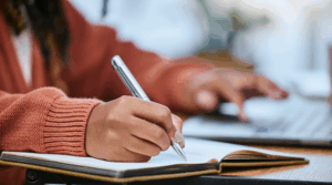 Woman using her laptop and writing notes in a journal 